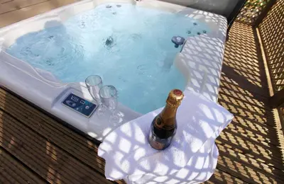 a hot tub with a bottle of champagne and glasses at Brook Lodge in Colchester