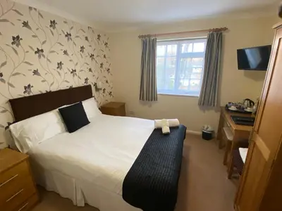 a bedroom with a bed and a desk and a window at Zaheer's Hotel in Baldock