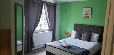 a bedroom with a bed with green walls and a window at Stansted Airport Lodge in Takeley