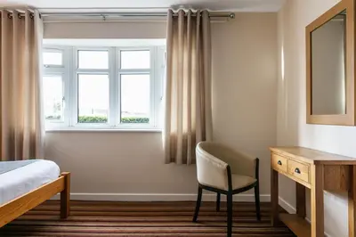 a bedroom with a bed and a chair and a window at Roydon Marina Village Hotel in Roydon