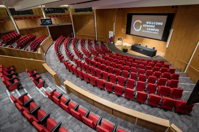 an auditorium with red chairs and a stage at Hinxton Hall Hotel and Conference Centre in Hinxton