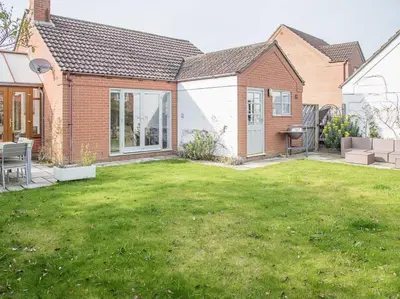 a backyard of a house with a grass yard at Honeybee Cottage, Orford in Orford