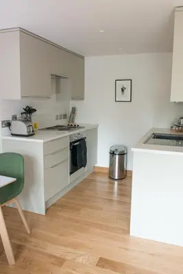 a kitchen with white cabinets and a green chair at West Court- Jesus College in Cambridge