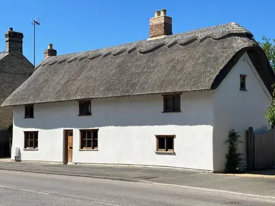 a white house with a thatched roof on a street at Orchard Cottage in Willingham