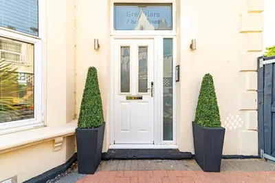 a white front door of a house with two bushes at Greyfriars in Clacton-on-Sea
