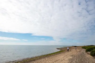 two people walking on a beach near the water at Mersea Island by Away Resorts in Colchester