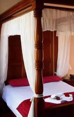 a wooden canopy bed with white curtains and red sheets at The Griffin Hotel in Attleborough