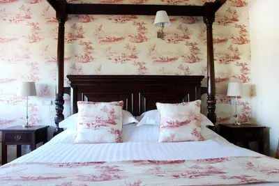 a bedroom with a bed with red floral wallpaper at The Pheasant Public House & Hotel in Gestingthorpe