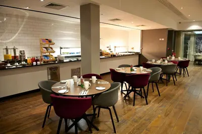 a restaurant with tables and chairs and a kitchen at Holiday Inn Southend by IHG in Southend-on-Sea