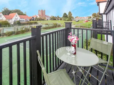 a table and chairs on a balcony with a tennis court at 1 Bell Lodge, Thorpeness in Thorpeness