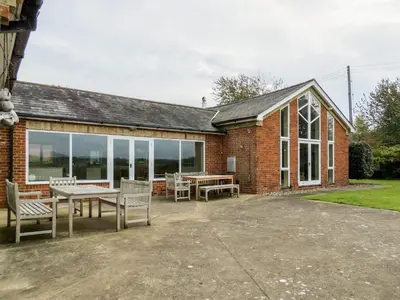 a brick building with a patio with tables and chairs at Crossing Cottage, Thorpeness in Thorpeness