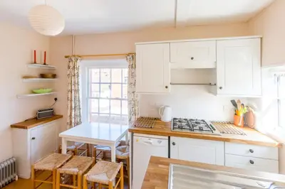 a kitchen with white cabinets and a table with chairs at 5 Coastguard Cottages in Aldeburgh