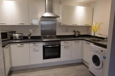 a kitchen with white cabinets and a washer and dryer at Meridian Apartment Suites in Southend-on-Sea