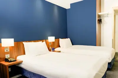 two beds in a hotel room with a blue wall at Holiday Inn Express Harlow by IHG in Harlow