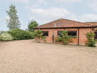 a brick house with a gravel driveway in front of it at Lowbrook Cottage in Diss