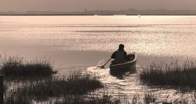 a person in a boat on the water with a paddle at Marsh View Cottage, Aldeburgh in Aldeburgh