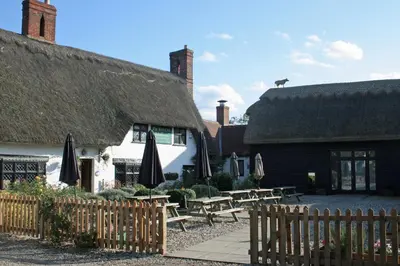 a pub with tables and umbrellas in front of a building at The Red Cow in Heydon
