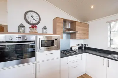 a kitchen with white cabinets and a clock on the wall at Horizon Lodge in Sizewell
