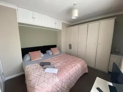 a bedroom with a bed with pink blanket and white cabinets at By Buildersbeds - Hill House 3 Bedrooms in Romford