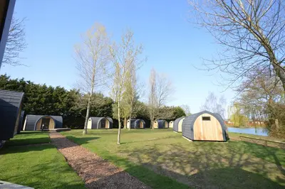 a group of tents in a field next to a lake at Camping Pods, Carlton Meres Holiday Park in Rendham