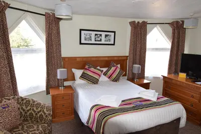 a bedroom with a bed and a chair and windows at Castle Lodge in Ely