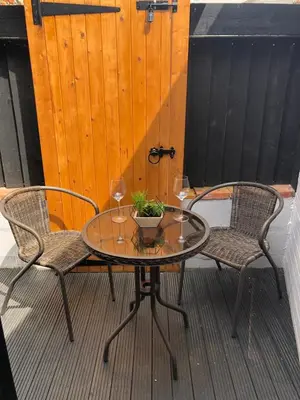 a glass table and two chairs on a patio at A quaint Wymondham cottage in Norwich