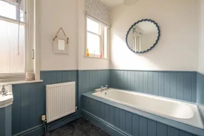 a blue bathroom with a tub and a mirror at Stoney Beach - Aldeburgh Coastal Cottages in Aldeburgh