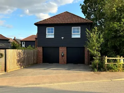 a black house with a garage in a driveway at Stansted Coach House - Apartment Hotel in Elsenham