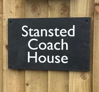 a sign for aasted coach house on a wooden fence at Stansted Coach House - Apartment Hotel in Elsenham