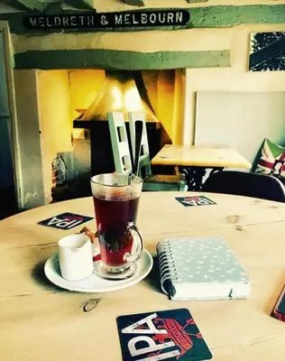 a cup of tea on a table with a book at The British Queen, Meldreth in Meldreth