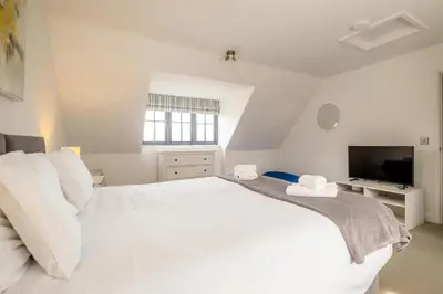 a white bedroom with a large bed and a tv at 5 Oakes Court in Thorpeness