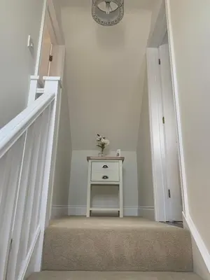 a stairway with a table and a clock on the wall at Hideaway Cottage in Halesworth