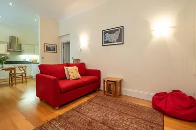 a living room with a red couch and a kitchen at Polly's - Aldeburgh Coastal Cottages in Aldeburgh