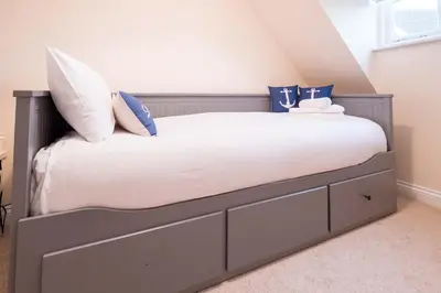 a bedroom with a bed with white sheets and blue pillows at Pinky Cottage in Aldeburgh