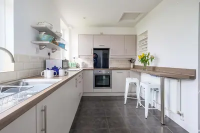 a kitchen with white cabinets and a counter with stools at Beaver Cottage in Aldeburgh