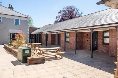 a patio with two wooden benches in front of a building at Three Tuns Apartments - Hazel - Aldeburgh Coastal Cottages in Pettistree