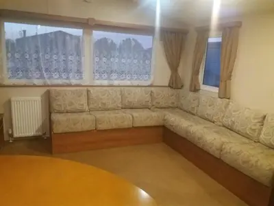 a couch in a living room with two windows at 2013 Willerby Sunset Static Caravan Holiday Home in Clacton-on-Sea