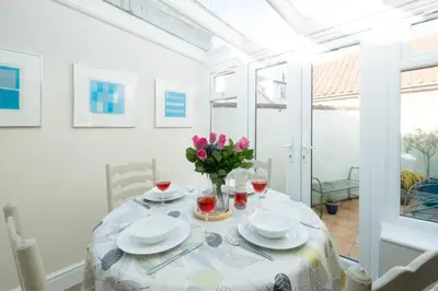a white dining room with a table with flowers on it at Admiral Cottage in Aldeburgh