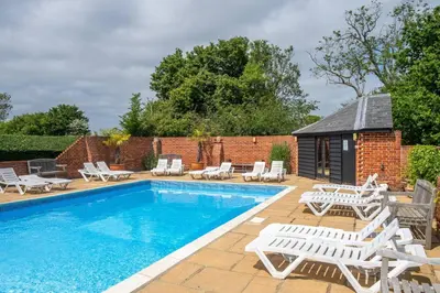 a swimming pool with lounge chairs and a building at East Green Farm Cottages - The Old Stables in Saxmundham