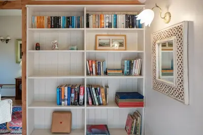 a book shelf filled with books next to a mirror at The Stables, Theberton in Theberton