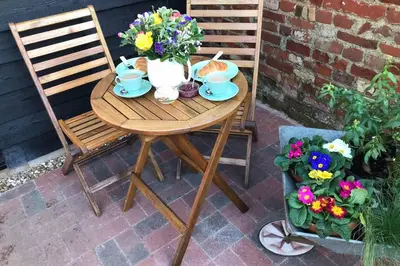 a wooden table and chairs with flowers on a patio at Melford Allotment Shed-Vintage Lodge Suffolk in Long Melford