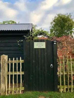 a black gate with a sign on it next to a fence at Melford Allotment Shed-Vintage Lodge Suffolk in Long Melford