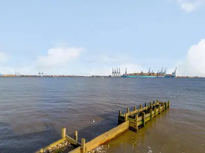 a dock in the water with a ship in the distance at Mayflower Cottage in Harwich