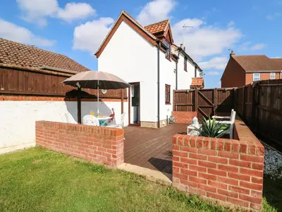 a wooden deck with an umbrella in a backyard at Chalk Cottage in Thetford