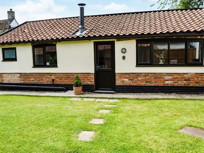 a house with a black door and a grass yard at The Bothy in Hockham