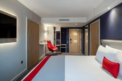 a hotel room with a bed and a red chair at Holiday Inn Express Cambridge West - Cambourne by IHG in Cambridge