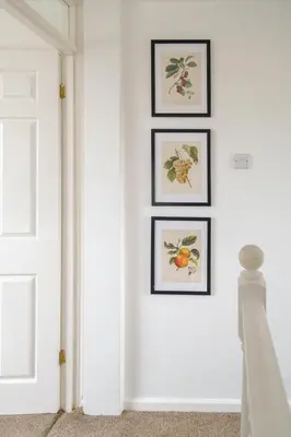 a white hallway with three framed paintings on the wall at Kittiwake, Aldeburgh - Aldeburgh Coastal Cottages in Aldeburgh
