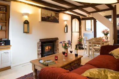a living room with a couch and a table with a fireplace at Meddlars a historic cottage on the countryside edge of a vibrant Market Town in Hadleigh