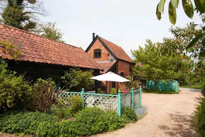 a house with a blue fence and an umbrella at Queenies, an authentic Rural Style coastal cottage in a Nature Reserve in Farnham