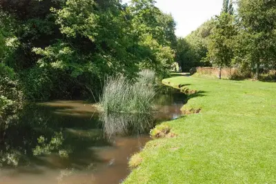 a river with trees and grass next to a field at The Old Monkey, a quirky bolthole on the edge of a historic Market Town in Hadleigh